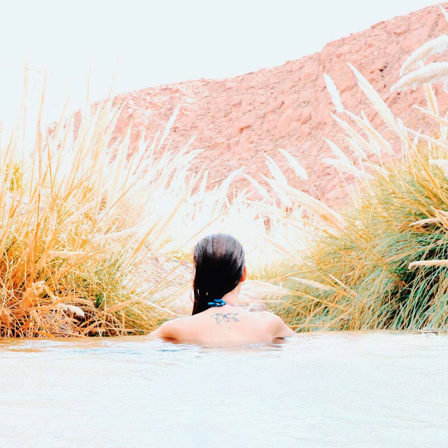 Mulher com tatuagem de um mapa-mundi nas costas, em uma piscina rodeada por plantas