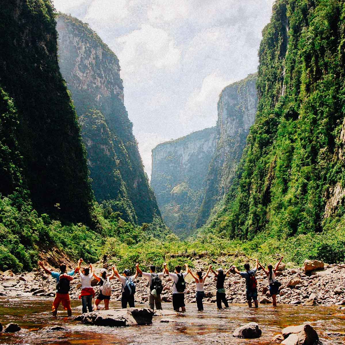 Um grupo de turistas de mãos dadas para o alto no meio das formações rochosas