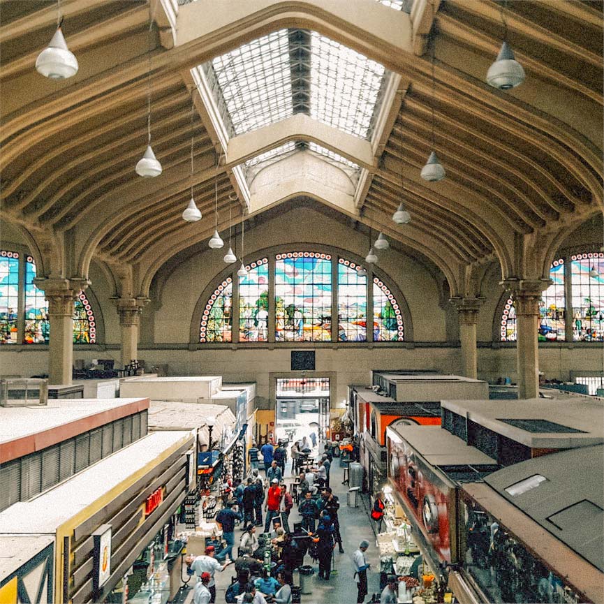 Visão de cima do Mercado Municipal de SP, com pessoas passando e lojas no piso térreo