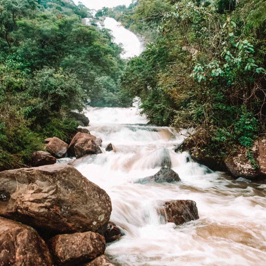 Cachoeira com queda pequena e extensa com muitas pedras ao arredor