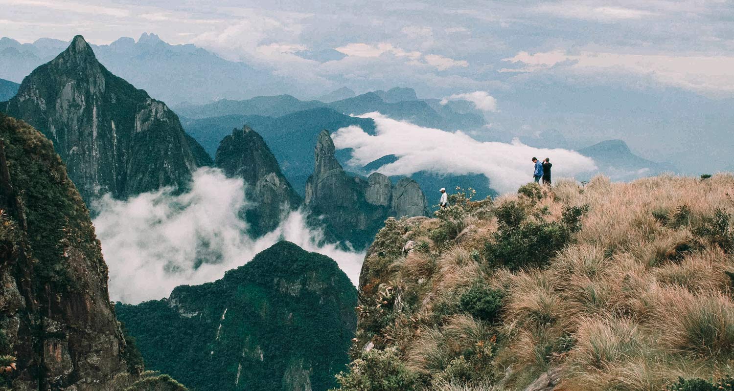 Três pessoas observando a vista panorâmica do Parque Nacional da Serra dos Órgãos, acima das nuvens 