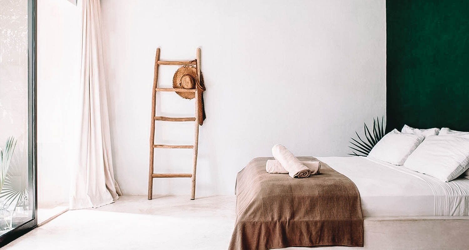 Quarto minimalista com cama ao centro, parede verde e escada em madeira de decoração
