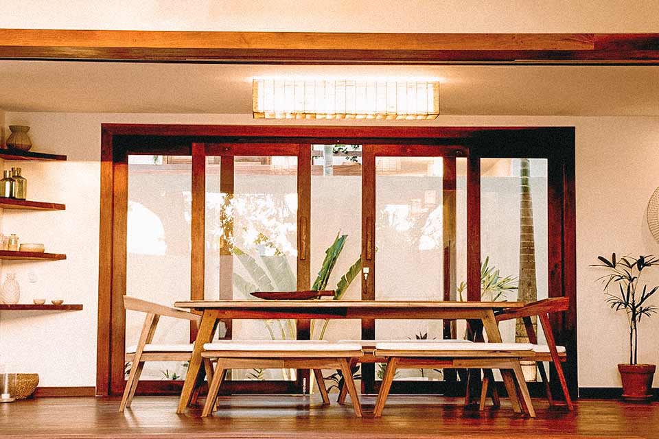 Mesa retangular de madeira com portas de vidro ao fundo, em casa em Jericoacoara