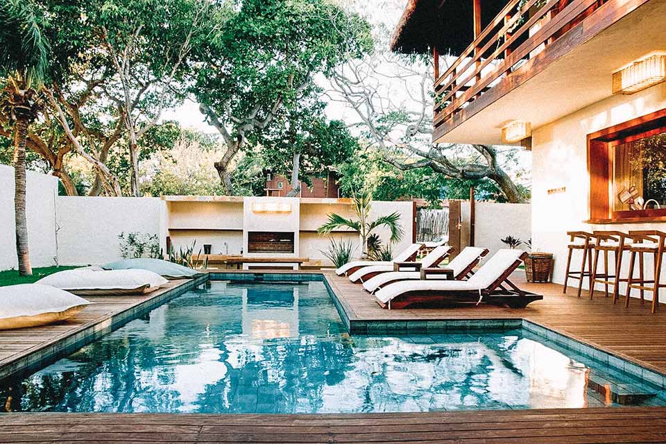 Piscina com cadeiras de sol e almofadões ao redor dentro de uma casa, em Jericoacoara