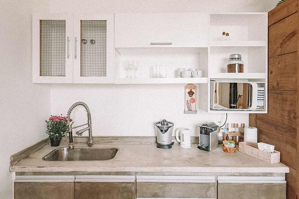 Cozinha com pia, armários brancos, microondas e alguns utensílios de cozinha