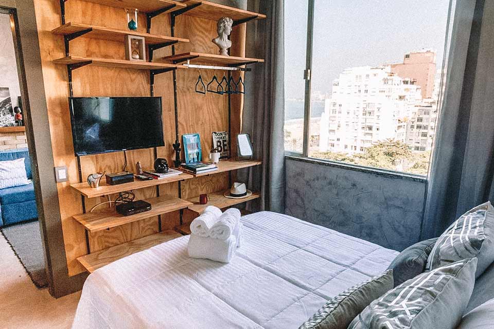 Quarto com janela vista mar, cama de casal e televisão