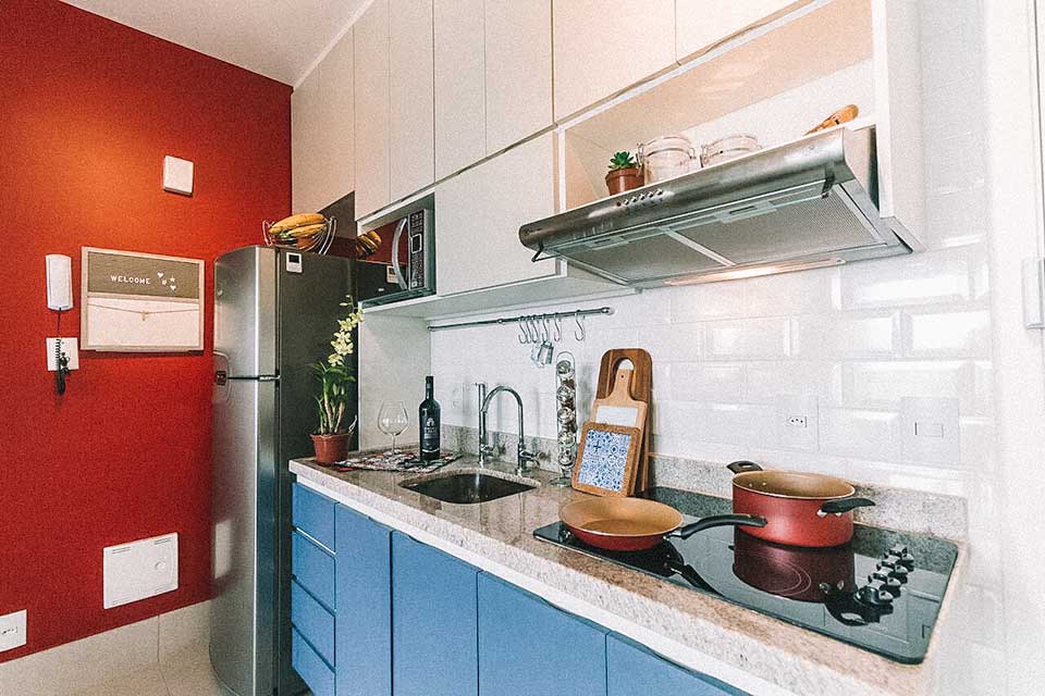 Cozinha com uma das paredes vermelhas, cooktop, pia, coifa e armário azul