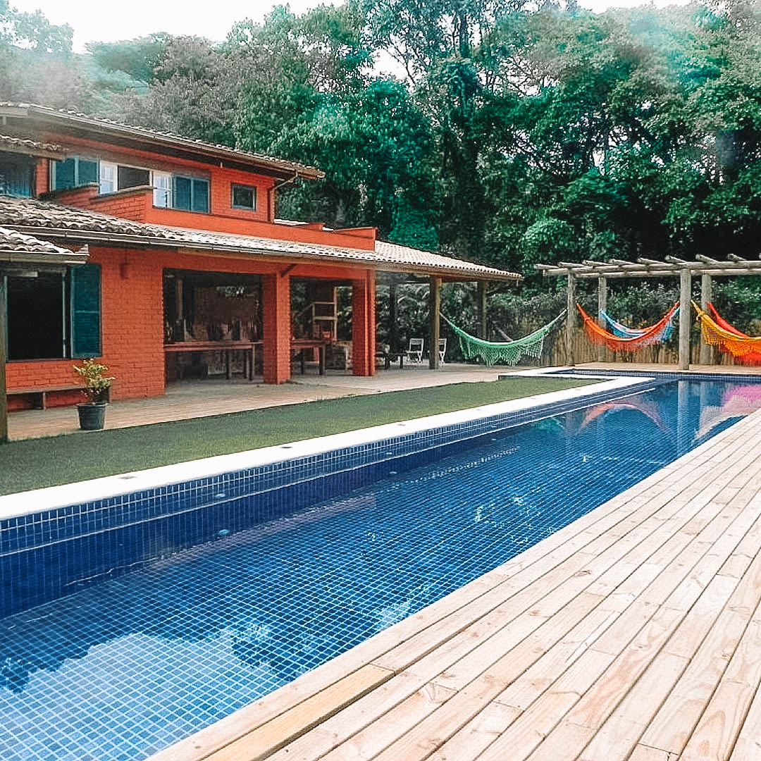 casa vermelha com grande piscina e redário ao lado