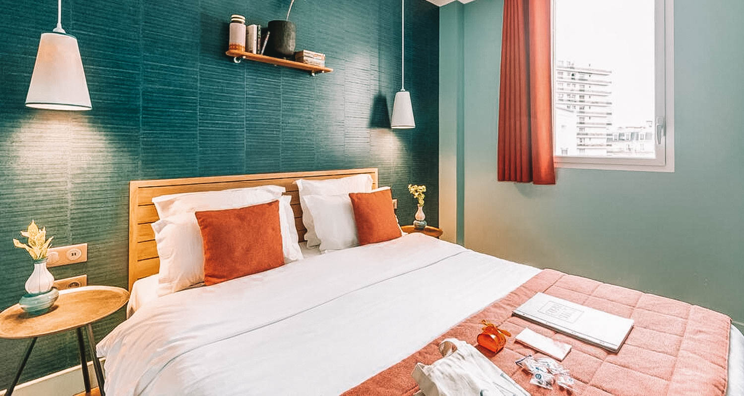 Quarto com cama de casal, parede azul, cortina laranja e almofadas laranja