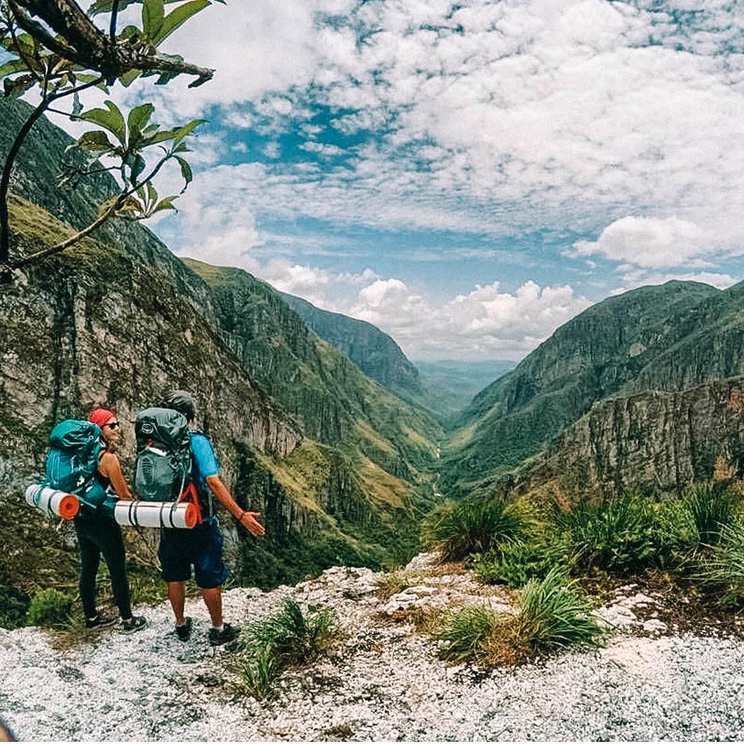 Duas pessoas com mochilões nas costas olhando para a vista do alto da montanha