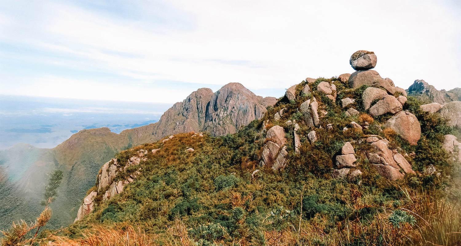 Monte coberto por vegetação, pedras soltas e uma paisagem do alto da montanha