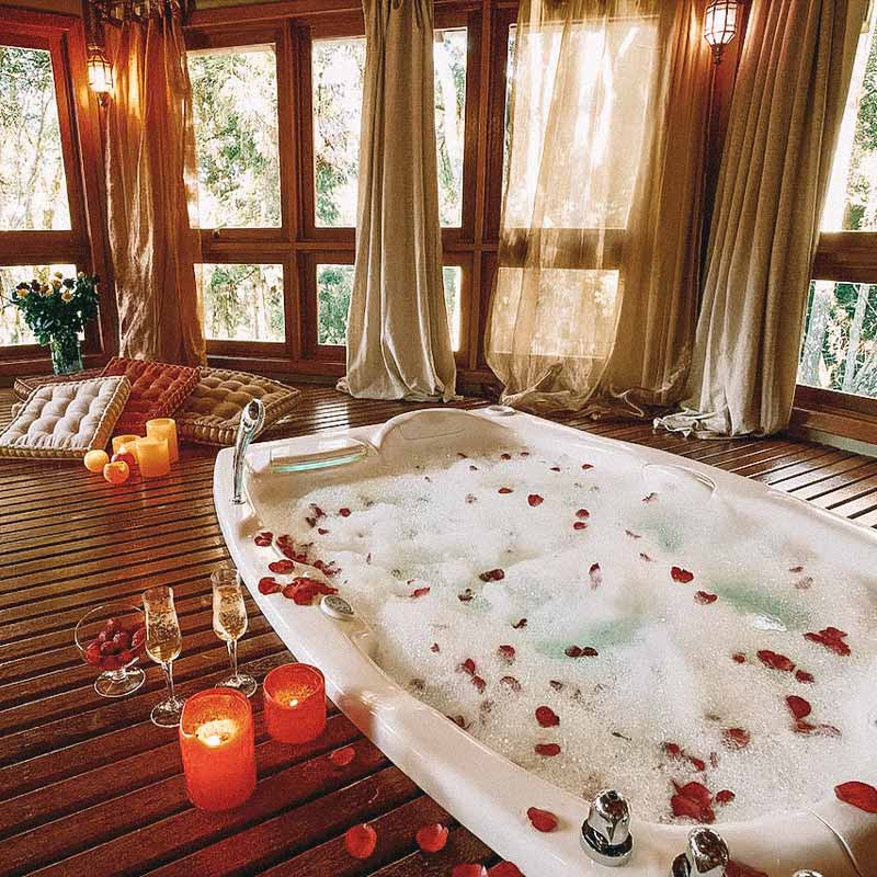 Banheira cheia decorada com rosas, com velas ao redor, em um deck de madeira romântica na Pousada Casa de Pedra, no Rio Grande do Sul
