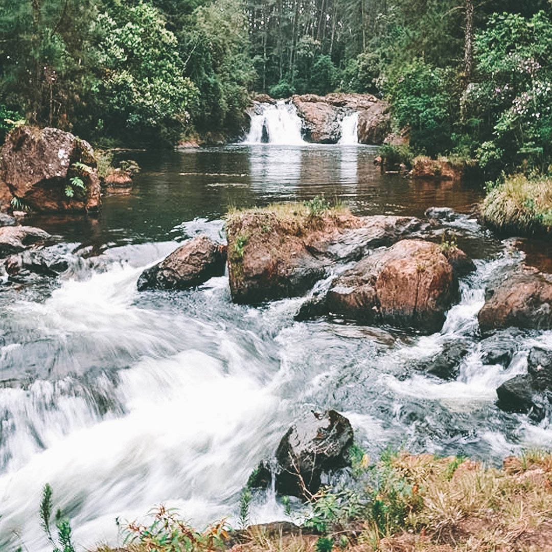 Pequena cachoeira com uma queda maior ao fundo e pedras no primeiro plano