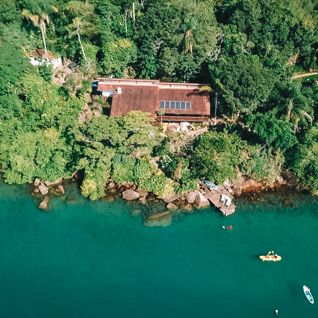 Foto aérea da vila, metade visão do mar e a outra a casa no meio da vegetação verde