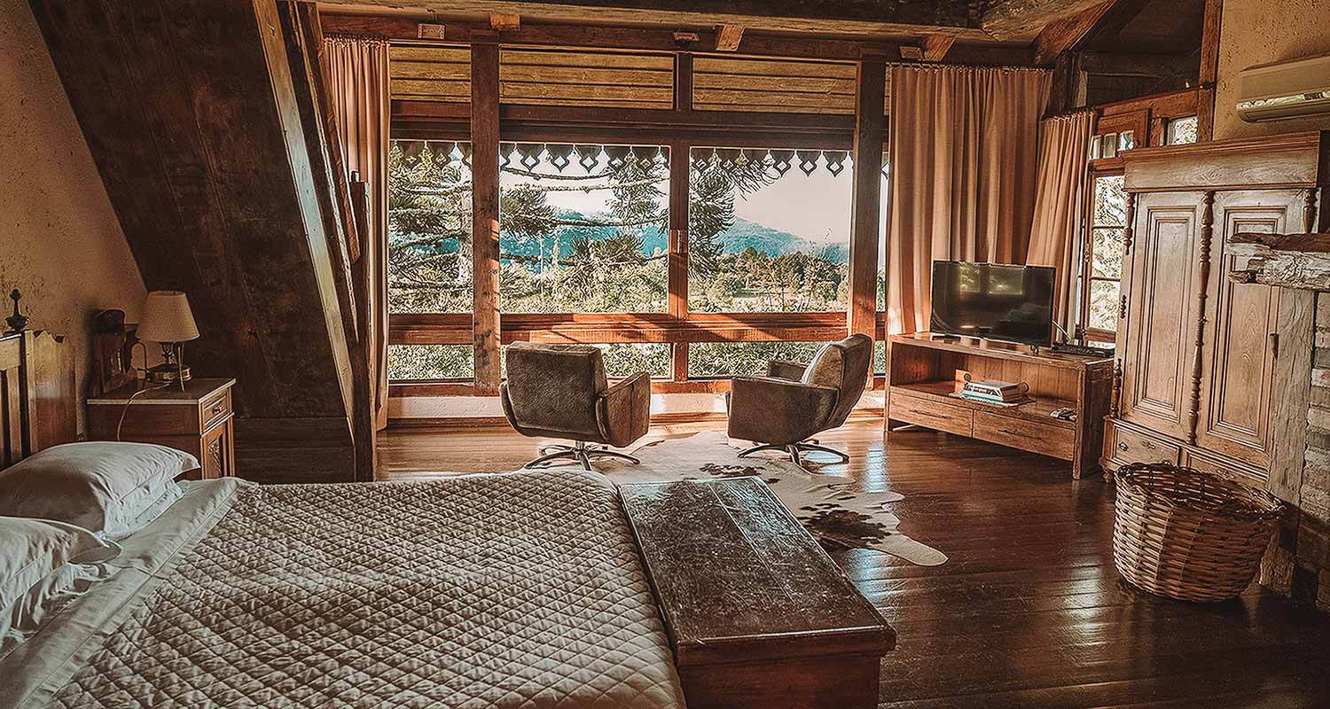 Quarto amplo, com cama de casal, poltronas, TV e vista para a mata nativa na Estalagem La Hacienda, no Rio Grande do Sul