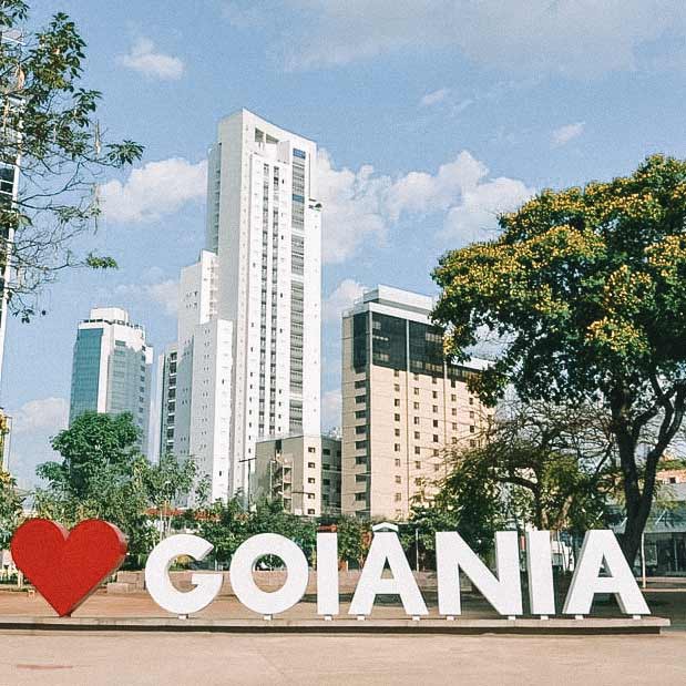 Placa com um coração vermelho e o nome Goiânia, instalado em um parque, com prédios ao fundo e árvores