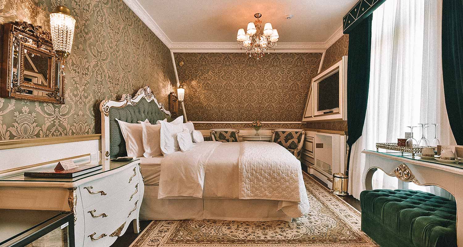 Quarto com decoração imperial, papel de parede, lustres, cama com cabeceira e tapete do Hotel Colline de France, em Gramado (Rio Grande do Sul)
