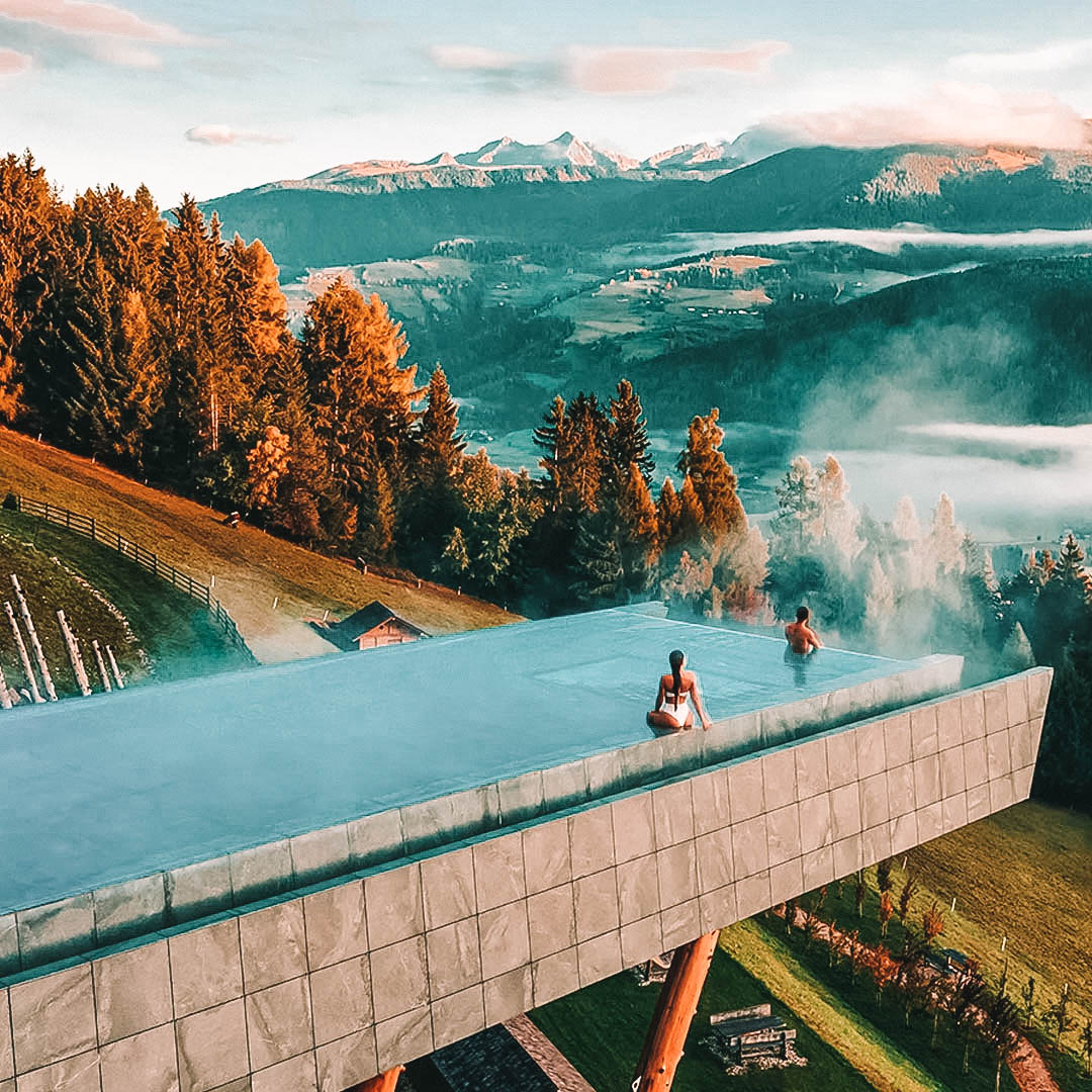 duas pessoas dentro de uma piscina com borda infinita com vista para o lago