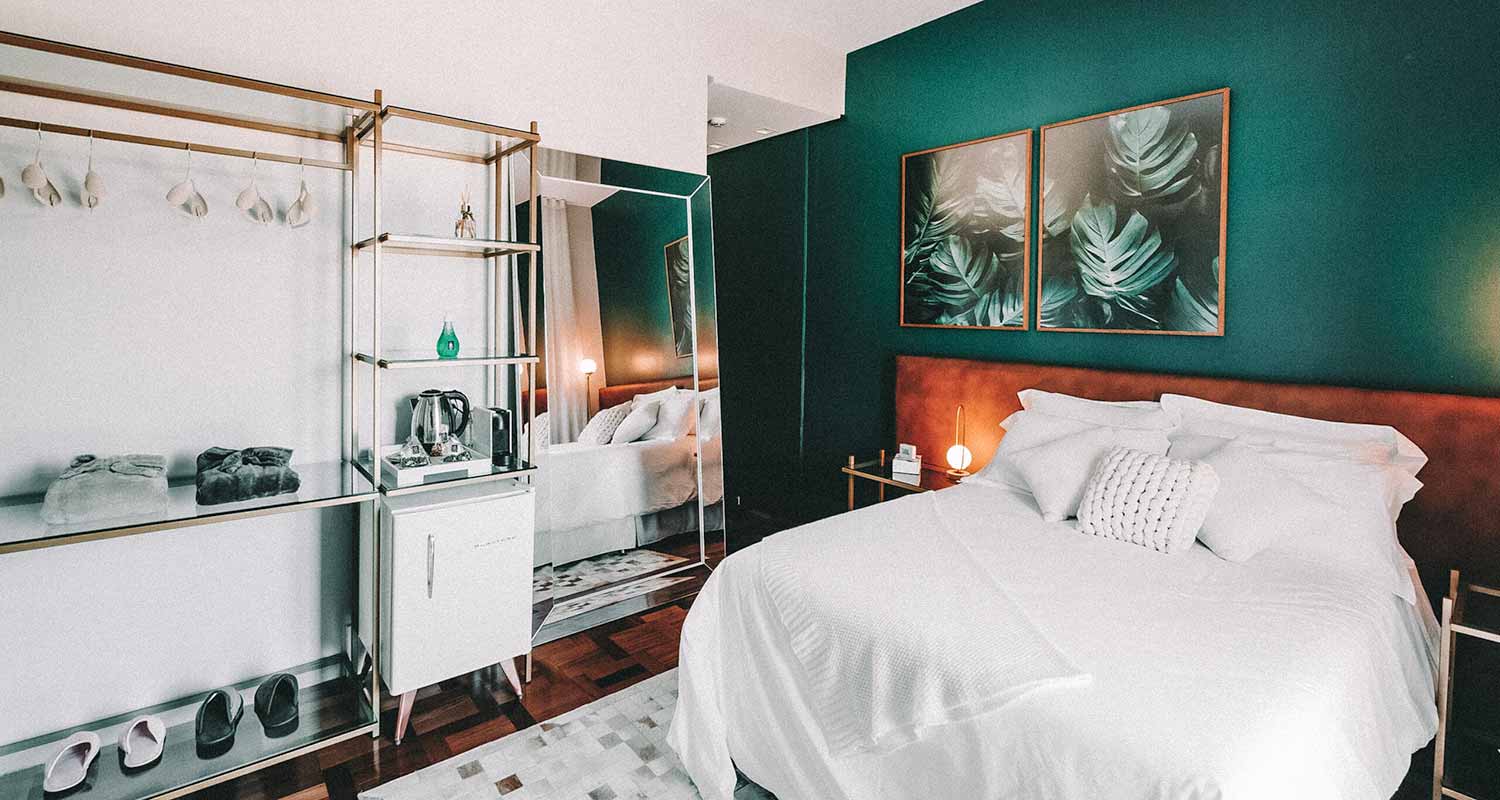 Quarto com paredes verdes, cama de casal com lençóis brancos e frigobar branco, no Lote20 Hotel Boutique, no Rio Grande do Sul