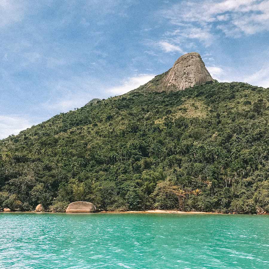 Morro do Pico, coberto por vegetação e rodeado pelo mar verde-turquesa, no Saco do Mamanguá