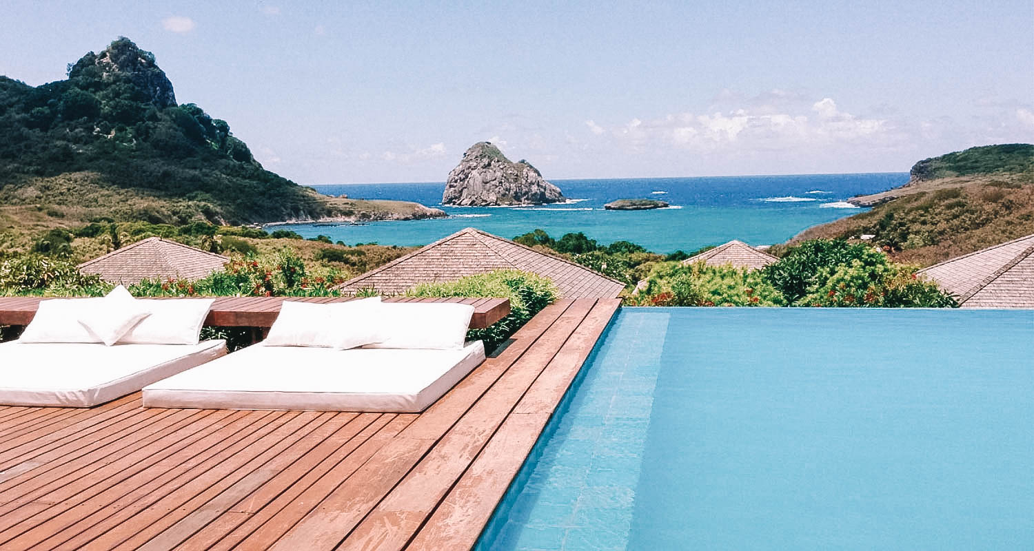 Piscina com borda inifinita com vista para o mar de Noronha e um deck de madeira ao lado com duas espreguiçadeiras