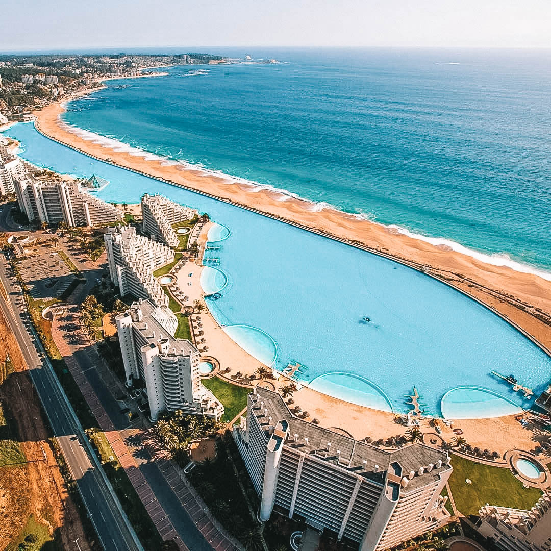 Vista aérea da maior piscina do mundo, com um quilômetro de extensão, rodeada por prédios e o mar