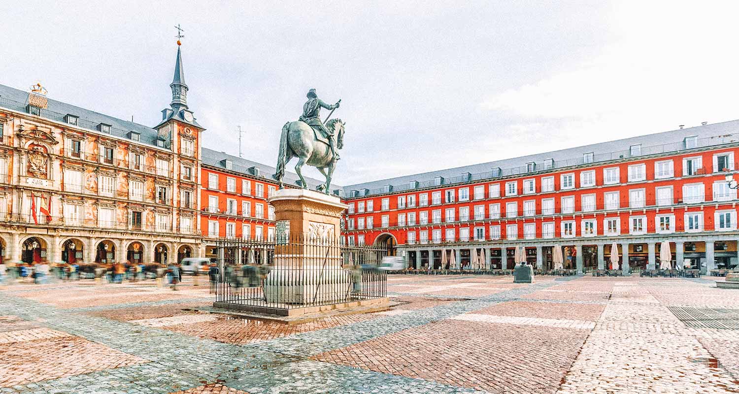 Plaza Mayor, com um prédio vermelho e amarelo ao fundo, e uma escultura com um homem montado em um cavalo, em Madri, uma das maiores cidades da Europa