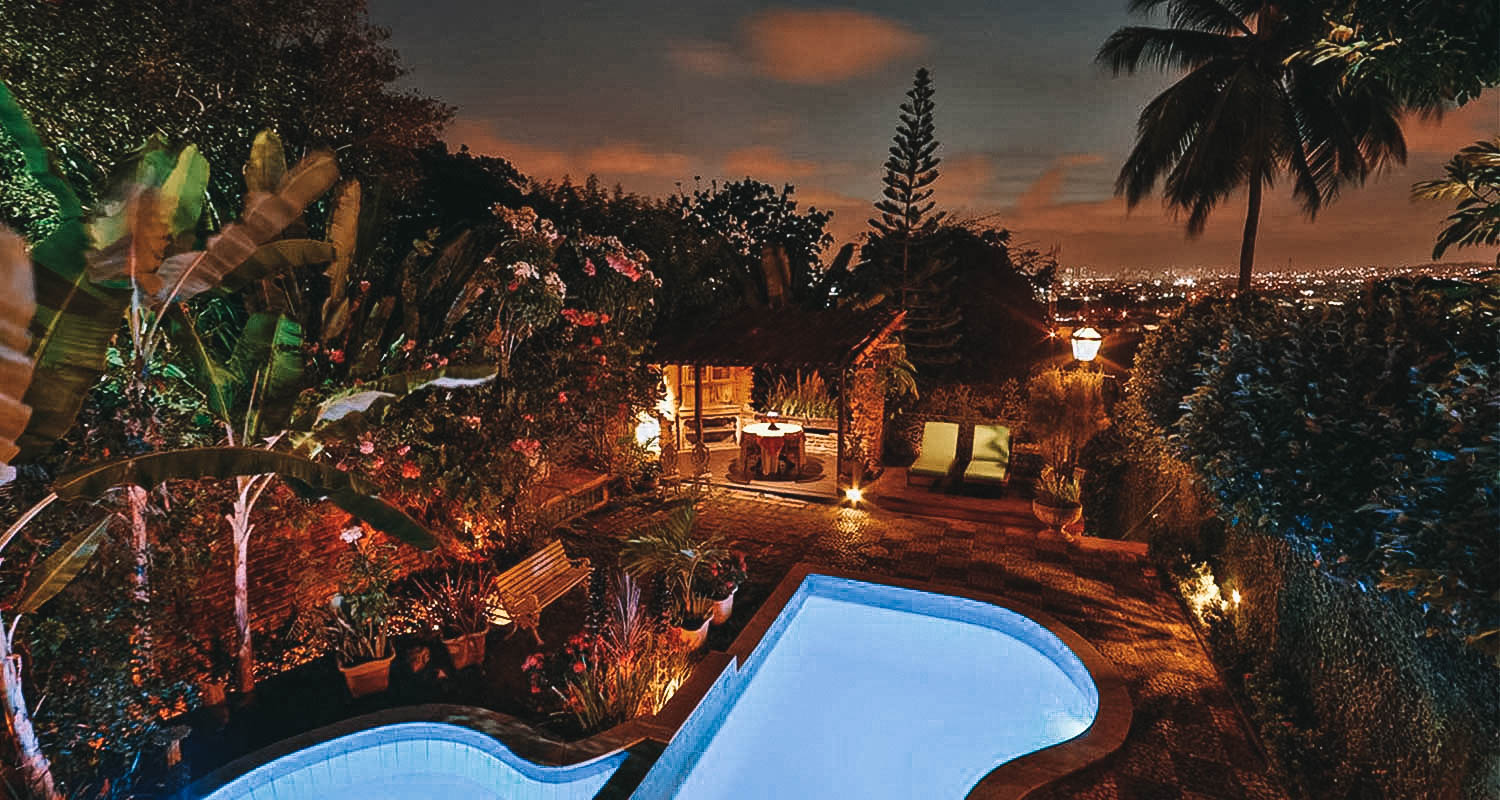 Vista aérea noturna do hotel, com piscina, muitas folhas e iluminação fraca