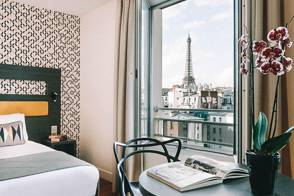 Quarto com uma mesinha com um livro aberto e uma janela com vista para a Torre Eiffel
