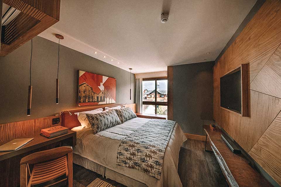 Quarto com parede de madeira, cama de casal e luminárias no Wood Hotel, em Gramado, no Rio Grande do Sul