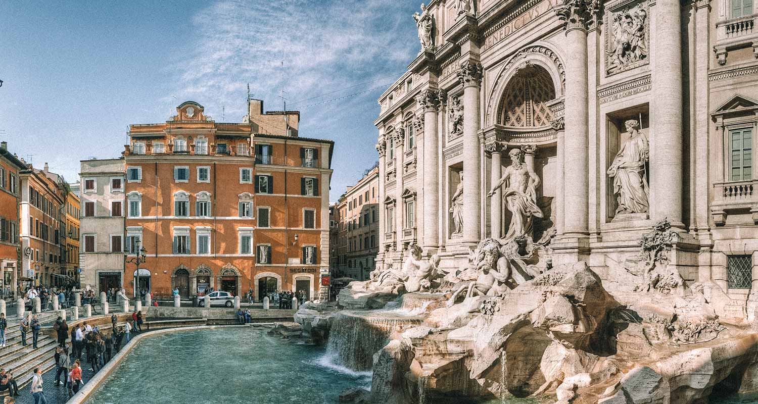 Fontana di Trevi na lateral e um prédio amarelo em segundo plano, ao fundo do monumento, em Roma, na Itália, oitava maior cidade da Europa