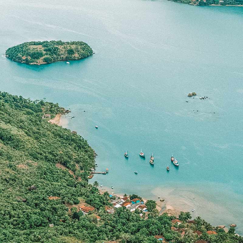 Mar com água de cor azul-turquesa, alguns barcos em uma costa litorânea do Saco do Mamanguá, em Paraty-Mirim
