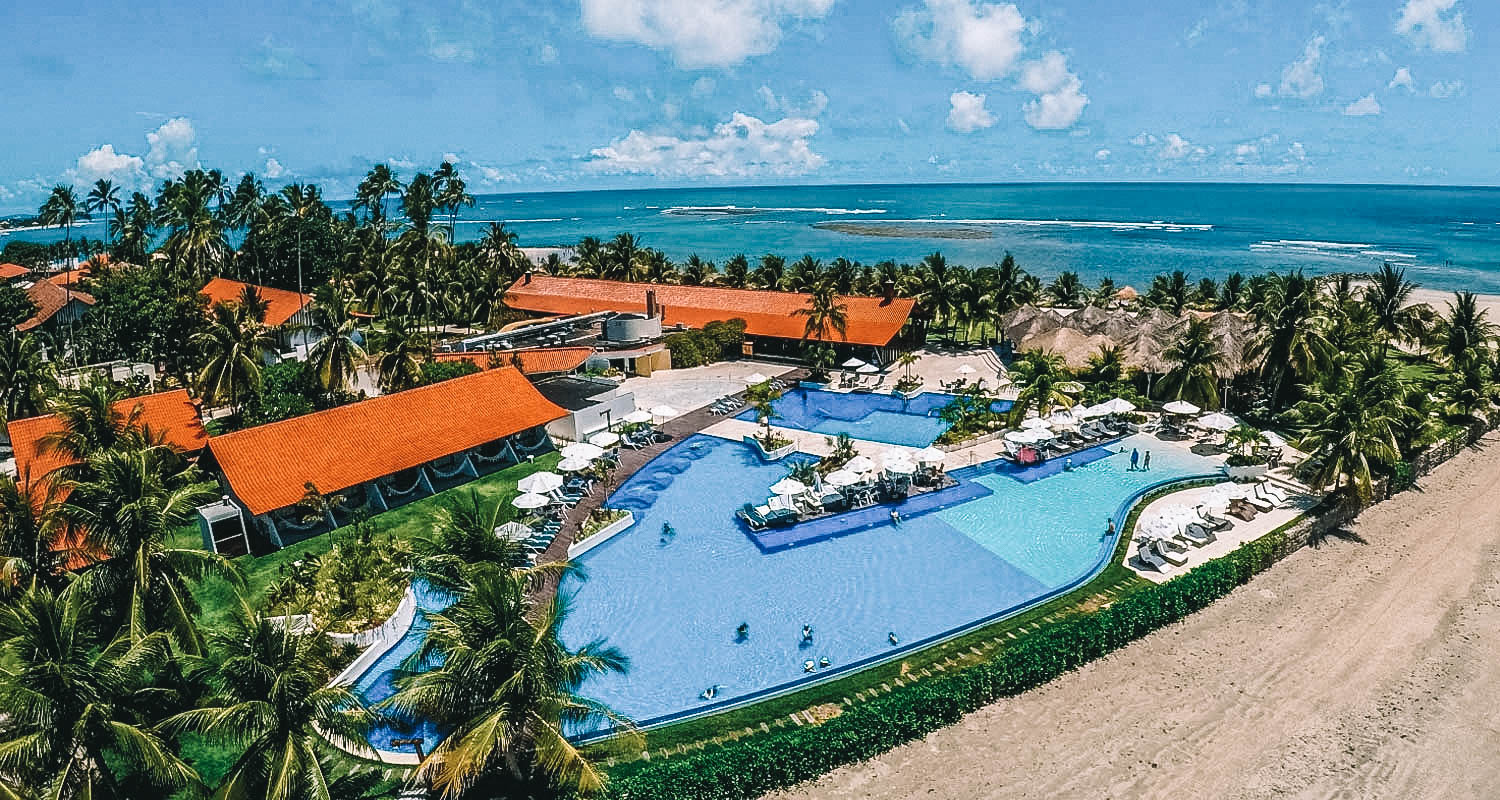 Vista aérea de todo o complexo do resort, abrangendo as acomodações, piscina, jardim e a vista beira-mar 