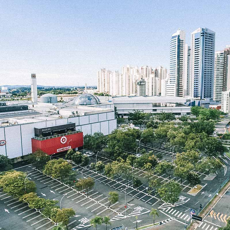 Vista aérea do estacionamento e da fachada do Shopping Flamboyant, com várias árvores e prédios ao redor