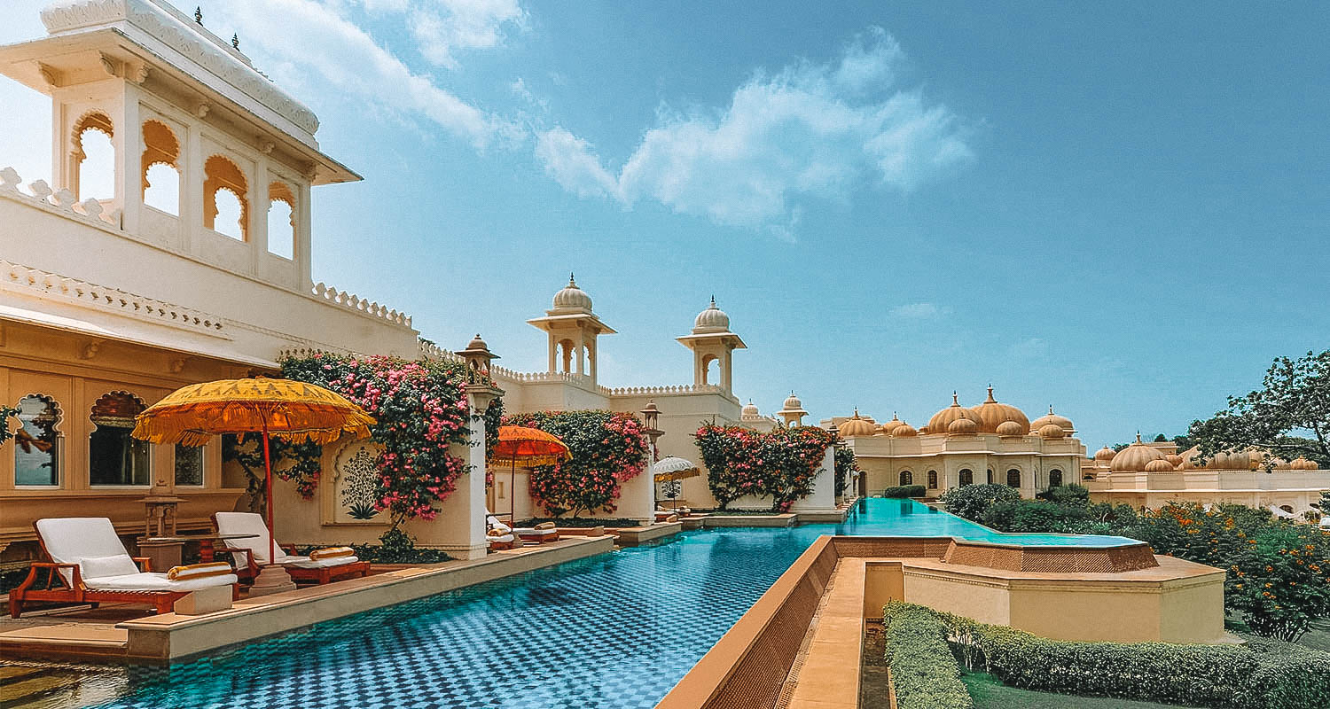 Piscina assimétrica com chão quadriculado, vista para o jardim e ligada ao quartos do palácio do The Uberoi