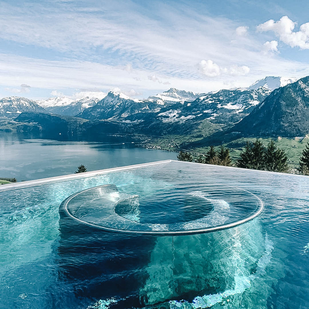 Piscina com borda infinita com uma banheira de hidromassagem dentro e vista para os alpes suíços cobertos por neve