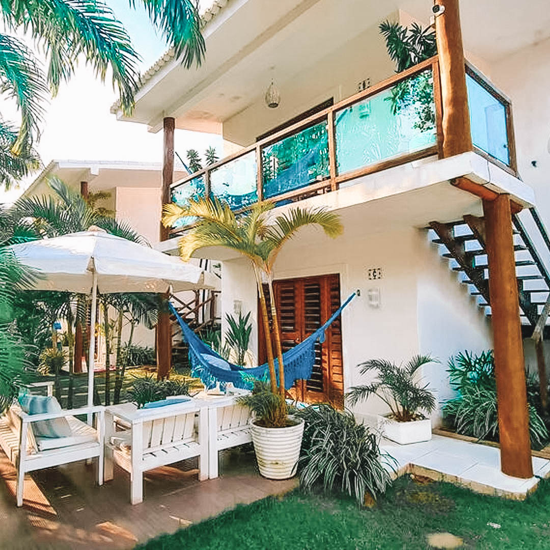 Casa branca de dois andares com pilares, portas e janelas em madeira, varanda e jardim