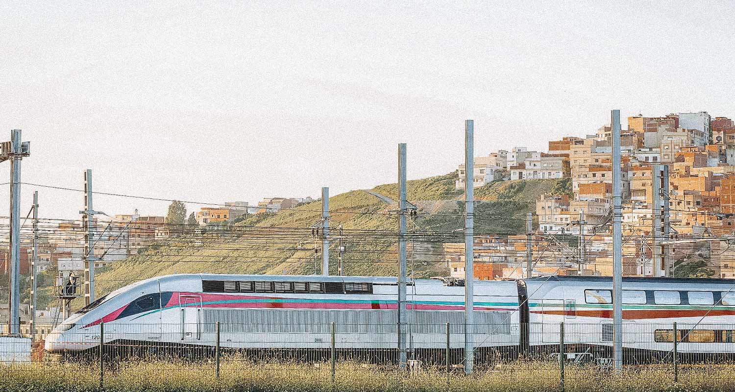 Trem passando no Marrocos, com cidades e morro ao fundo. Trens mais rápidos do mundo.