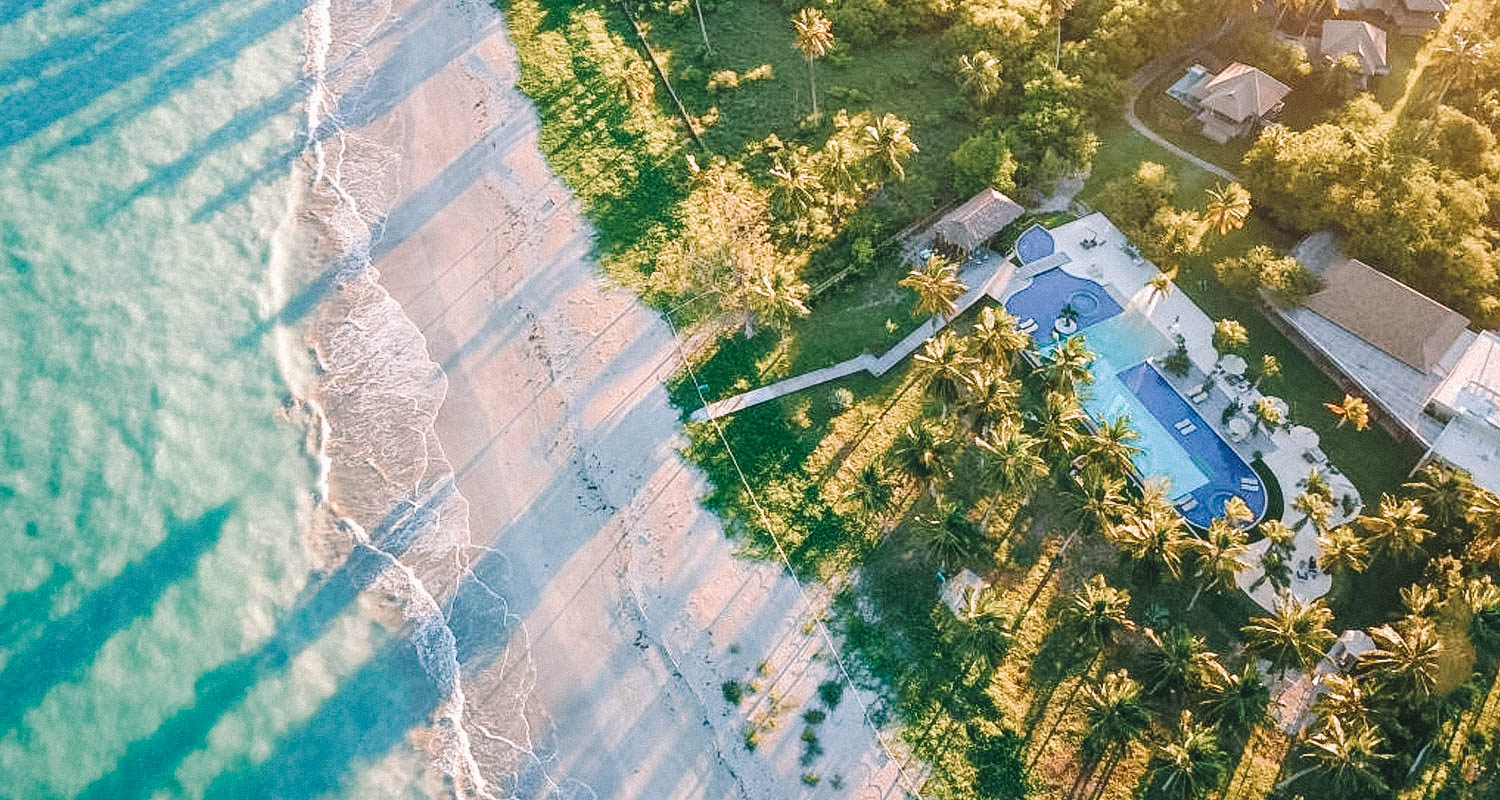 Vista aérea do mar em Alagoas, uma faixa de areia e um gramado, onde está a pousada