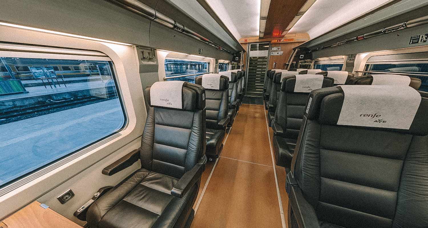 Interior de um trem, com carpete de madeira e poltronas pretas e couro