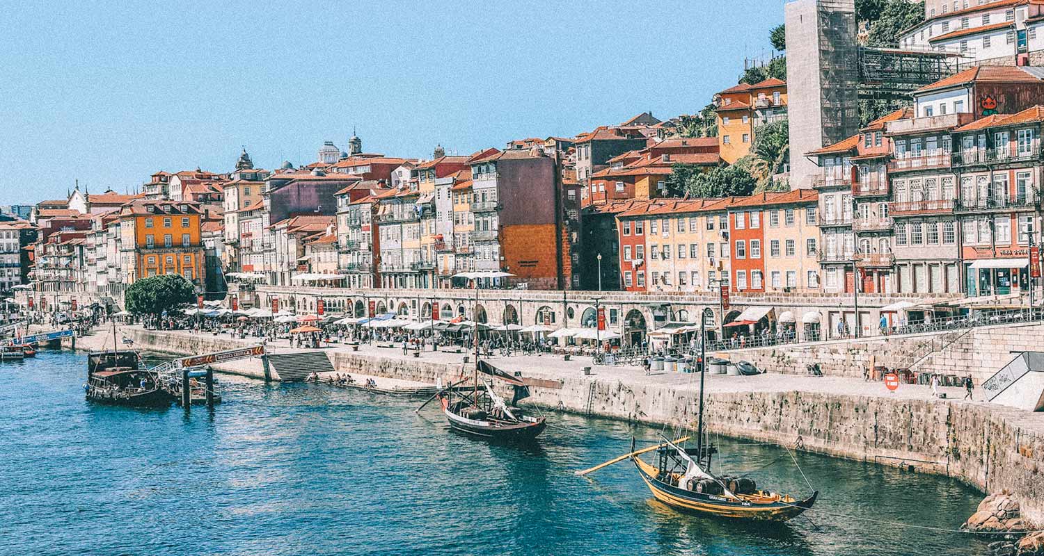Barcos em canal com prédios coloridos, na cidade de Porto, em Portugal