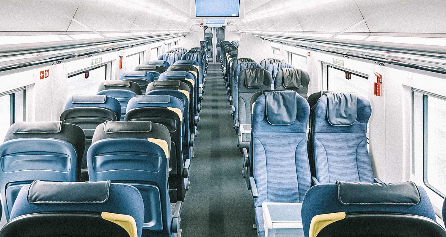 Interior de um trem com poltronas azuis e paredes brancas