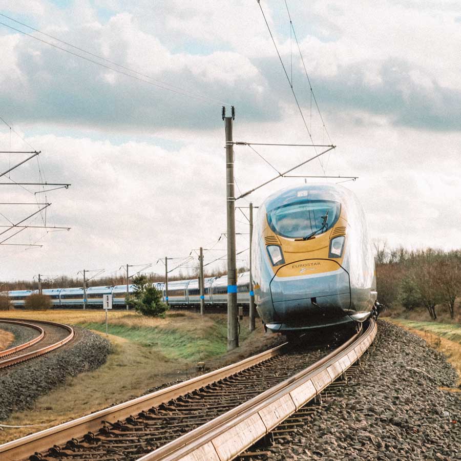 Visão frontal de um trem azul com detalhes amarelos passando pela ferrovia