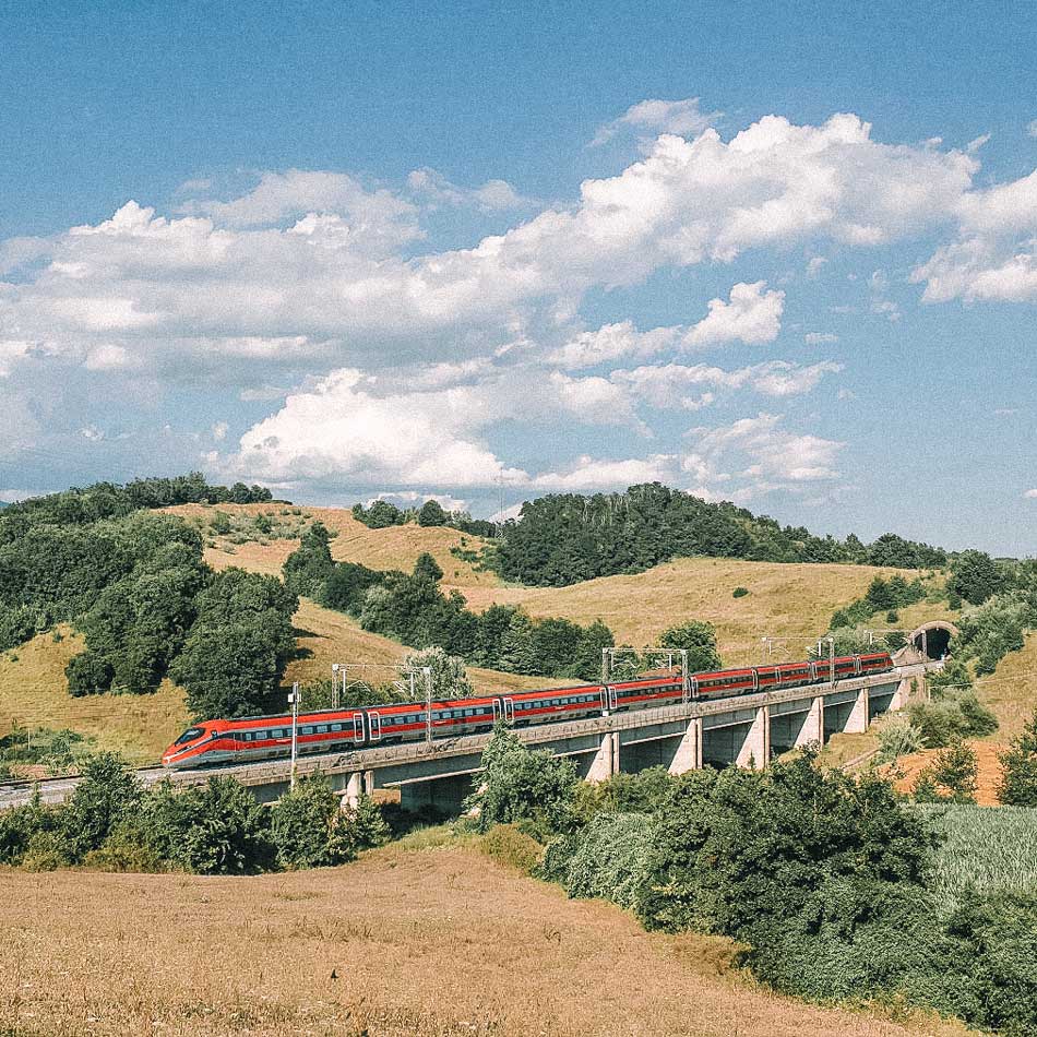 Trem vermelho passando por área serrana na Itália