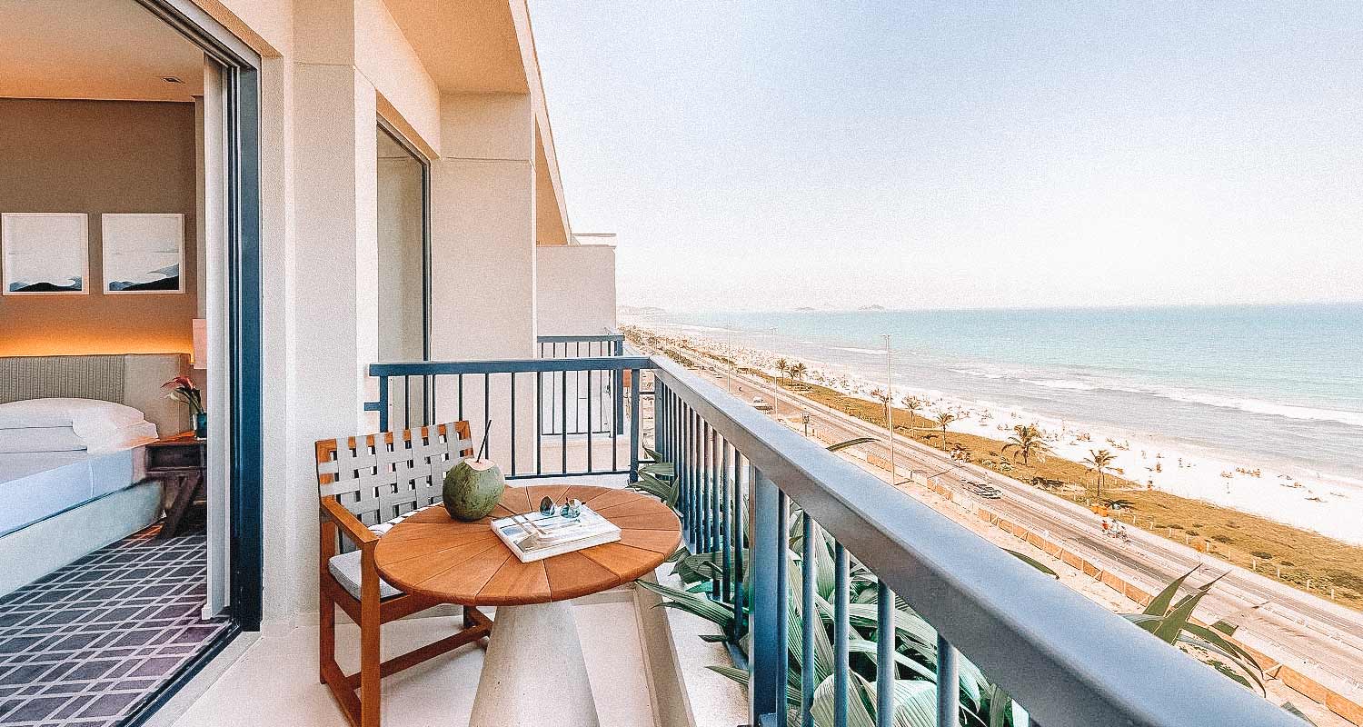 Varanda de quarto no Grand Hyatt, com vista panorâmica para a praia e uma mesinha e uma cadeira de madeira