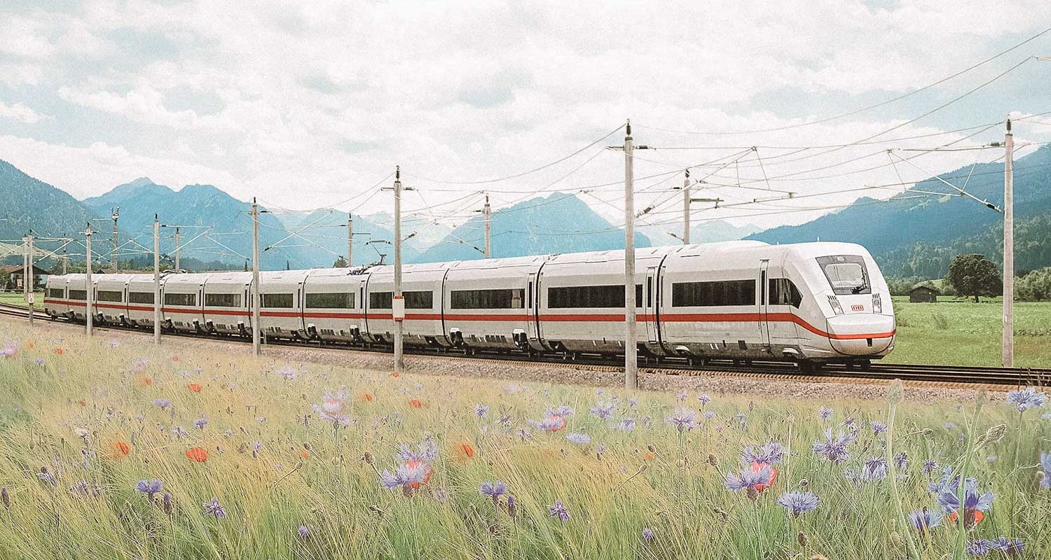 Trem-bala branco com detalhes vermelhos passando por uma ferrovia com montanhas ao fundo, na Alemanha