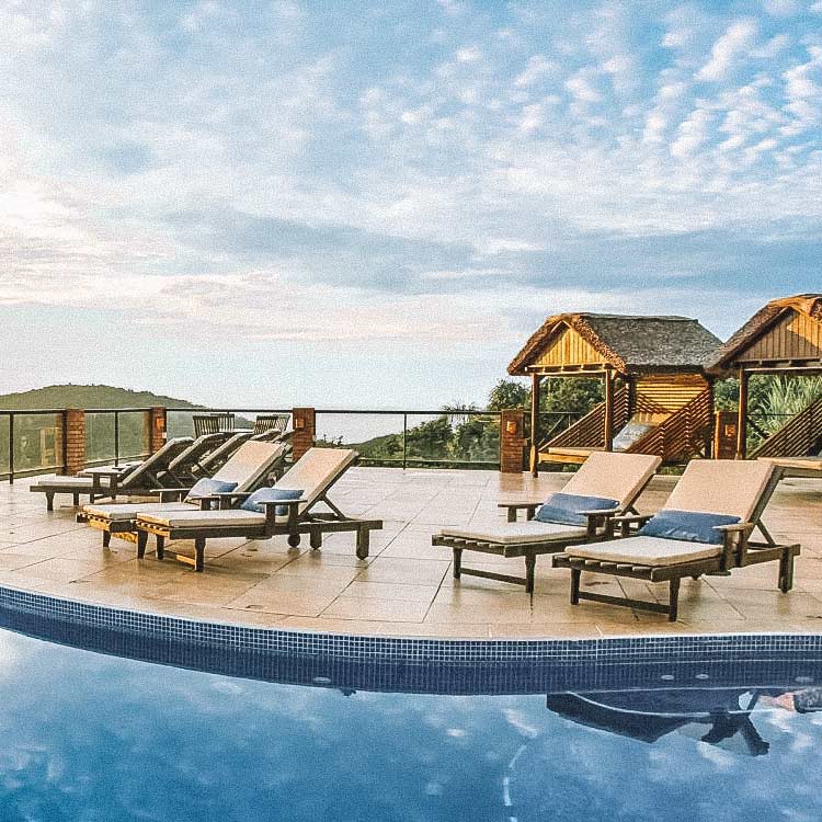 Cadeiras de sol do lado de uma piscina, bangalôs do lado e ao fundo, vista parcial da serra. Pousadas e hotéis em Santa Catarina.