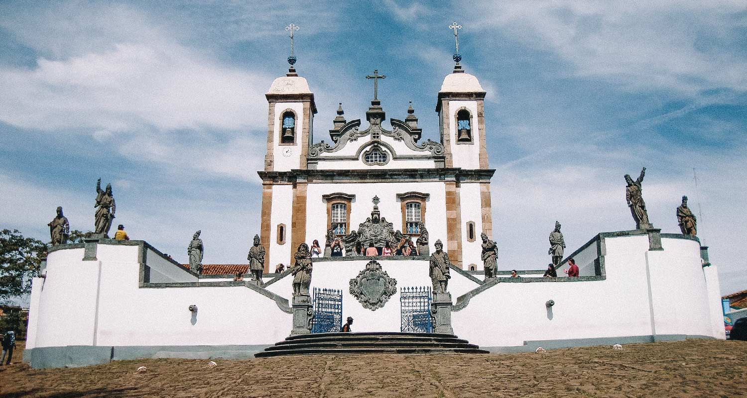 Fachada do Santuário Bom Jesus dos Matosinhoscom paredes brancos e detalhes em amarelo e ouro e esculturas de santo