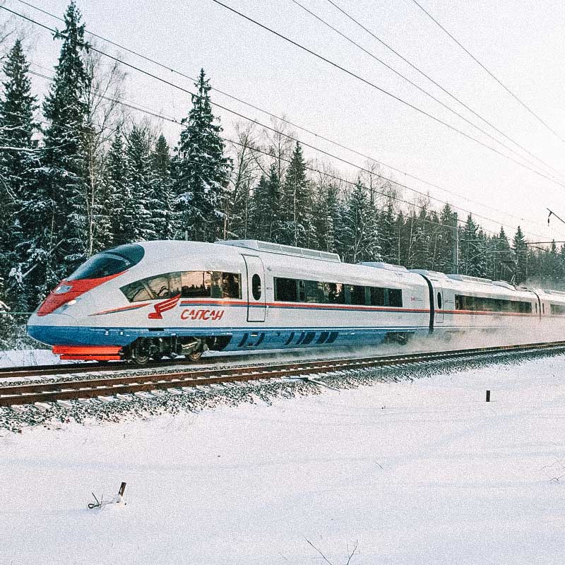 Trem passando por ferrovia com pinheiras ao fundo e chão com neve. Trens mais rápidos do mundo.