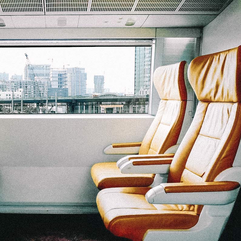 Bancos de couro alaranjado em trem, com janela com vista para a cidade. Trens mais rápidos do mundo.